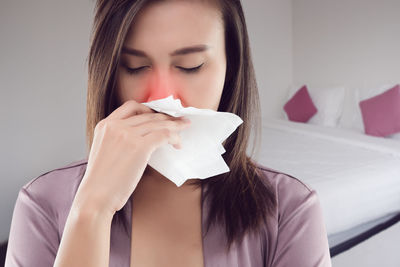 Close-up of young woman blowing nose with tissue paper at home