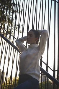 Low angle view of young woman standing against railing