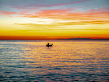 Silhouette people on sea against orange sky