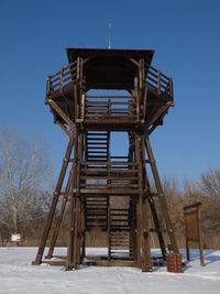 Low angle view of ladder on snow covered field against clear blue sky