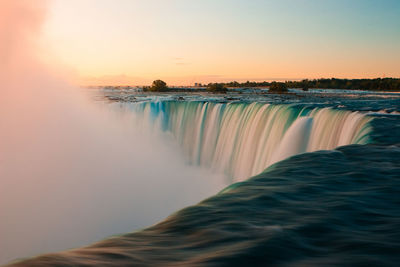 Scenic view of waterfall against sky during sunset