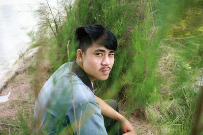 High angle portrait of young man sitting by plant on field