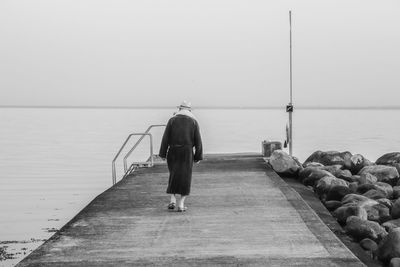 Rear view of man on pier over sea against sky