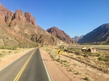 Road leading towards mountains against clear sky