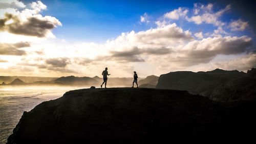 Silhouette people standing on rock against sky during sunset