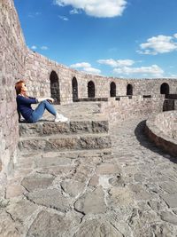 Man sitting in front of historical building against cloudy sky