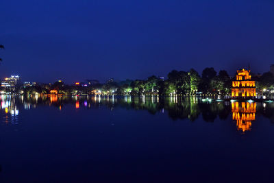 Reflection of illuminated buildings in lake against sky at night