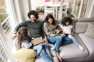 Happy father with mother and daughters reading book on sofa at home