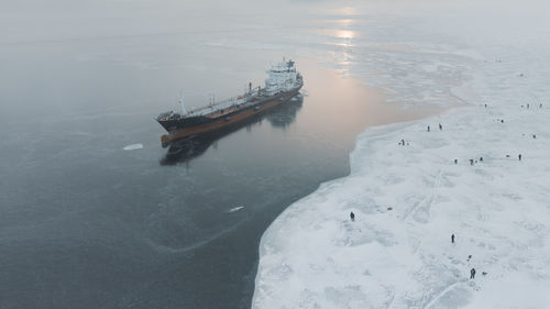 A group of fishermen on the surface of the frozen sea near an oil tanker. air view.