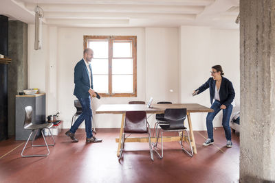 Carefree man and woman playing table tennis while standing at office