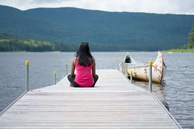 Rear view of woman relaxing on pier over sea against mountains