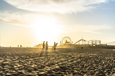 People at amusement park against sky during sunset