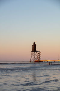 Tower on sea against clear sky during sunset