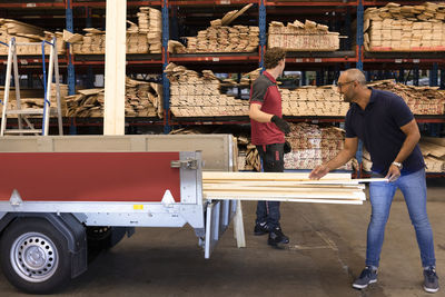 Mature man loading plank in vehicle trailer at hardware store