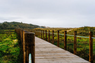 Wooden fence on footpath amidst field against sky