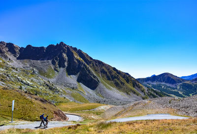 Man riding bicycle on rocky mountains against clear blue sky