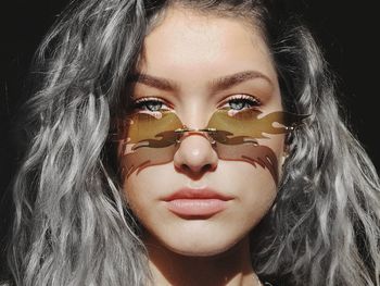 Close-up portrait of beautiful young woman wearing sunglasses against black background