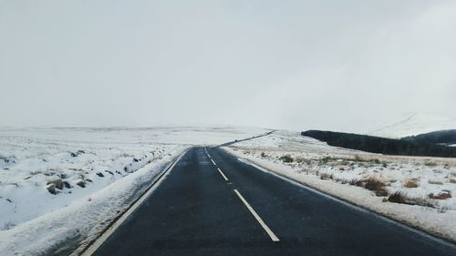 Road amidst snow covered field against sky