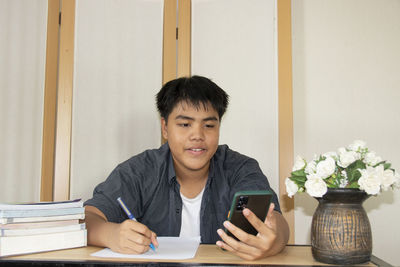 Portrait of young man using mobile phone while sitting on table