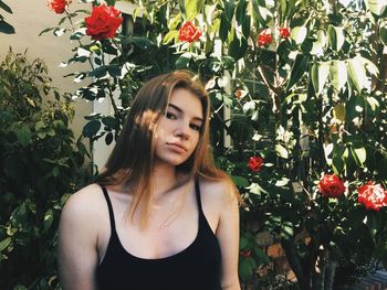 Portrait of young woman standing by plants at yard