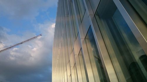 Low angle view of modern skyscraper against cloudy sky