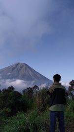 Rear view of man standing by mountain against sky