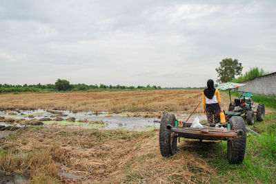 Rear view of man sitting on field against sky