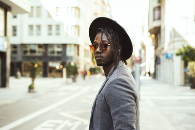 Side view of young man wearing sunglasses standing on road in city