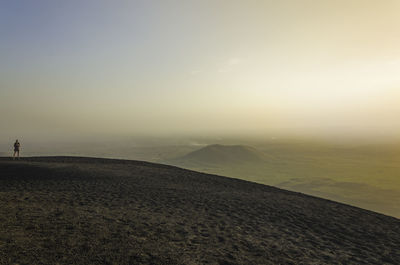 Mid distance view of woman standing at cerro negro against sky during sunset