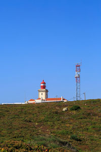 Lighthouse on field by building against clear blue sky