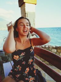 Young woman smiling while standing by sea against sky