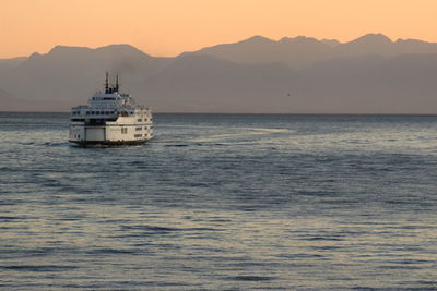 Ship sailing on sea against mountains during sunset