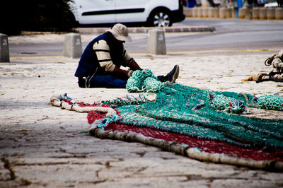 Man sitting by fishing net on footpath