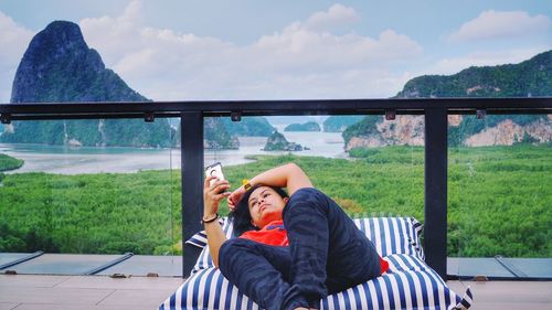 Mature woman using mobile phone while lying on mattress in balcony