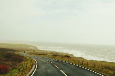 Empty road by sea against sky