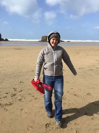 Portrait of smiling woman walking at beach against sky