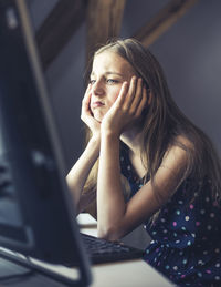 Thoughtful girl using computer while sitting on table