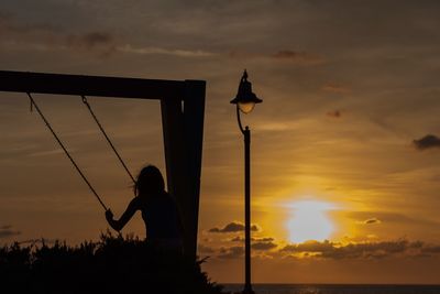 Silhouette man standing by pole against sky during sunset