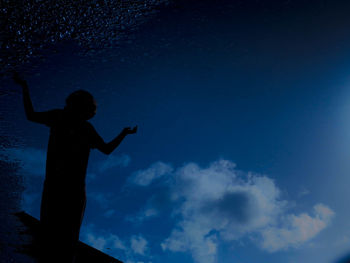 Silhouette person standing against blue sky reflecting on puddle