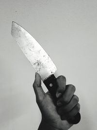 Close-up of hand holding knife against white background