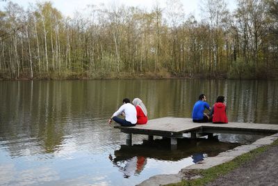 People sitting on boat in lake against trees