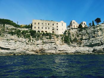 Buildings by sea against clear blue sky