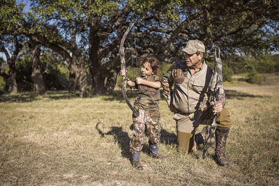 Girl aiming with arrow while father guiding on grassy field