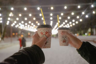 A walk in the winter, christmas lights are on, paper cups with warming drinks are in hand