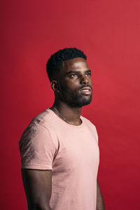 Portrait of young man looking away against red background