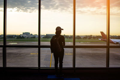 Rear view of woman looking at landscape while standing by window at airport