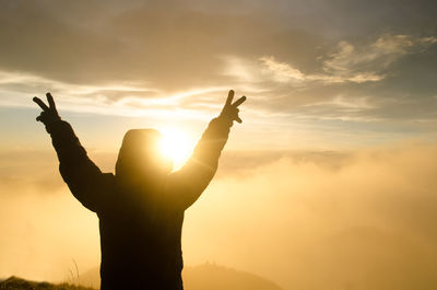 Silhouette man showing peace sign against sky during sunset