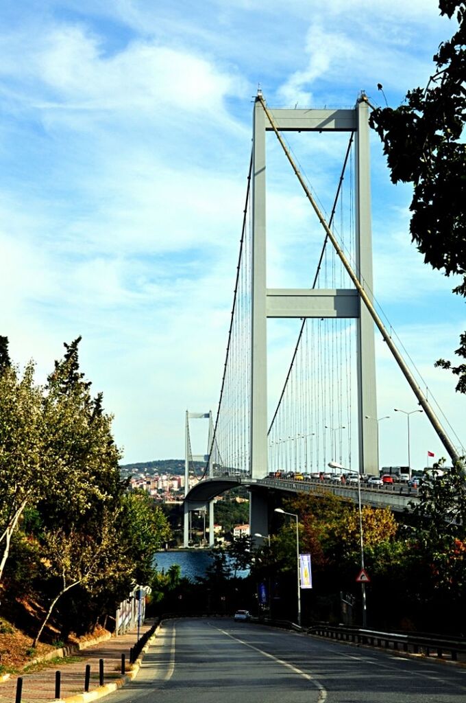 architecture, built structure, sky, connection, the way forward, transportation, bridge - man made structure, tree, building exterior, cloud - sky, diminishing perspective, road, cloud, city, engineering, bridge, vanishing point, cloudy, day, long