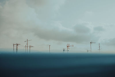 Low angle view of electricity pylons against cloudy sky