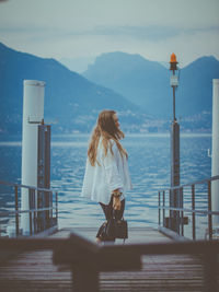 Woman standing on railing by sea against sky